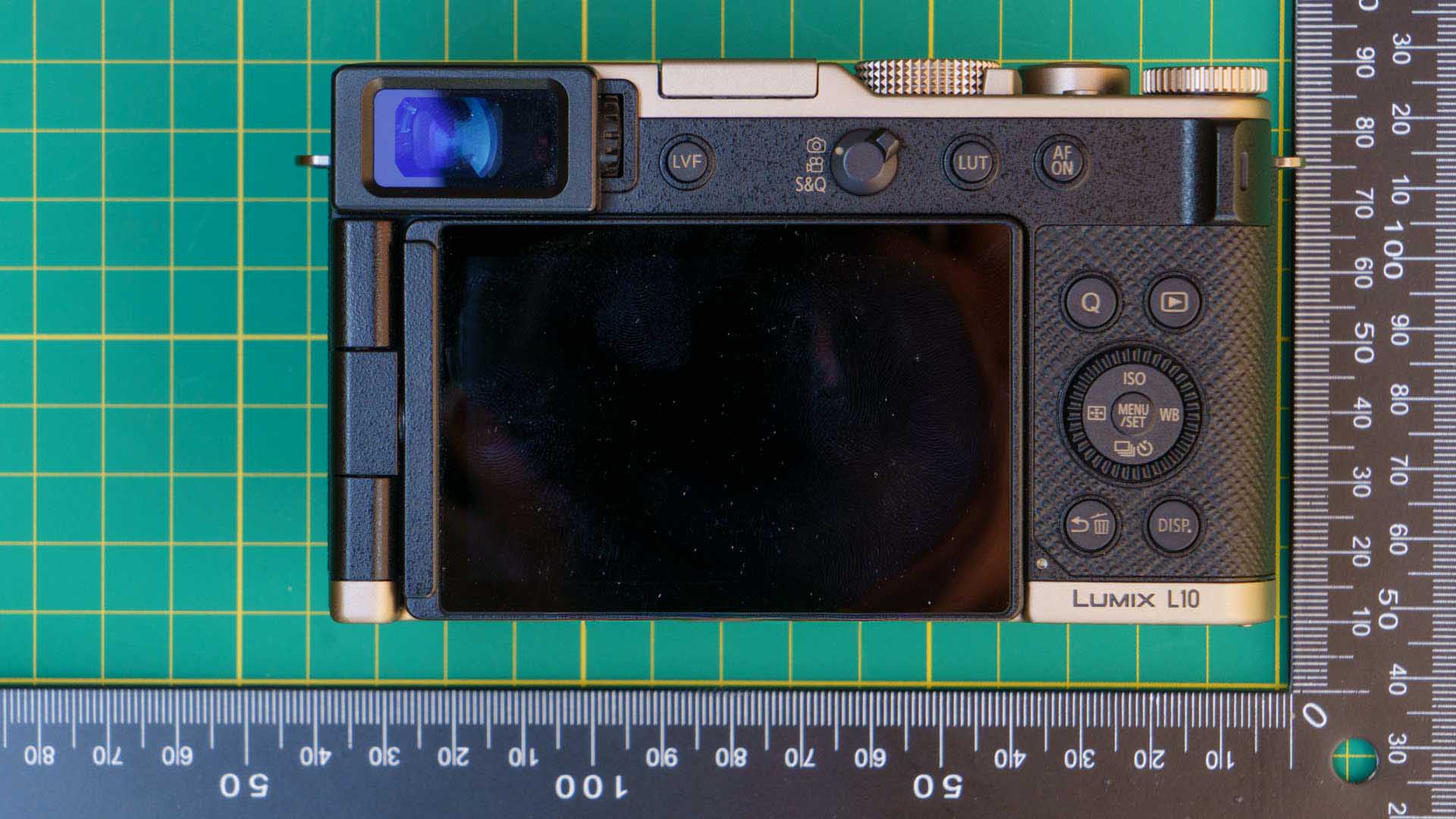 Top-down rear view of the Panasonic Lumix L10 on a cutting mat, highlighting the electronic viewfinder, screen, and rear controls.