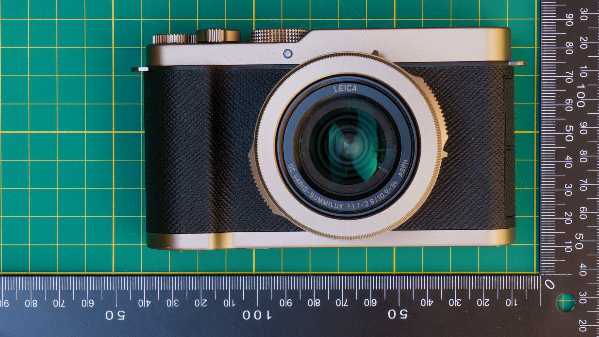 Top-down front view of the Panasonic Lumix L10 on a cutting mat, centered on the Leica-branded lens.