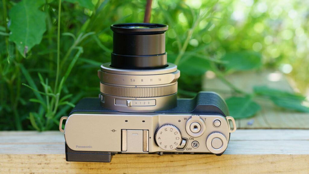 Top view of the Panasonic Lumix L10 with the lens extended upward, resting on a wooden surface outdoors.