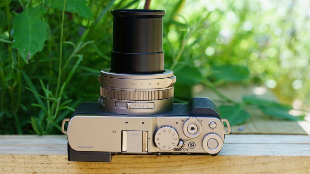 Top view of the Panasonic Lumix L10 with the zoom lens fully extended, photographed against a blurred green garden background.
