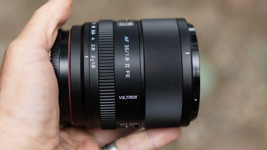Opposite side view of the Viltrox AF 35mm F1.8 II FE lens held in a hand, highlighting the focus ring, aperture ring, and Viltrox logo.