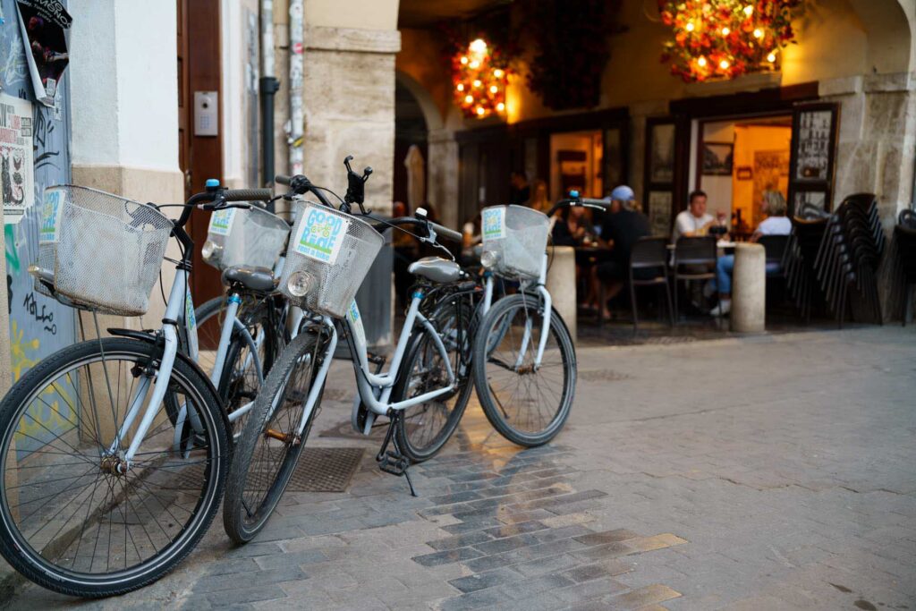 Three hire bicycles are parked outside a café in Valencia, where diners sit beneath warm decorative lighting.