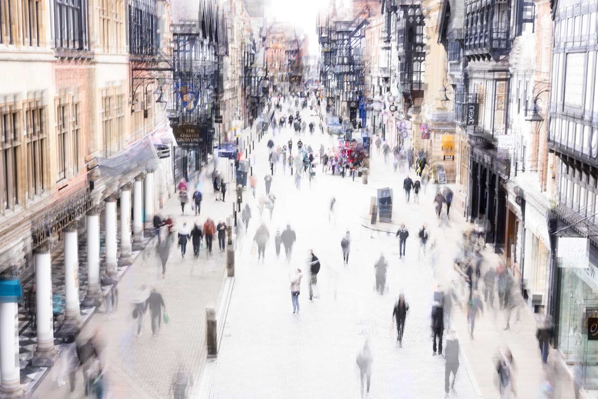Elevated view along a busy Chester shopping street, with historic black-and-white buildings and pedestrians blurred by a long exposure.