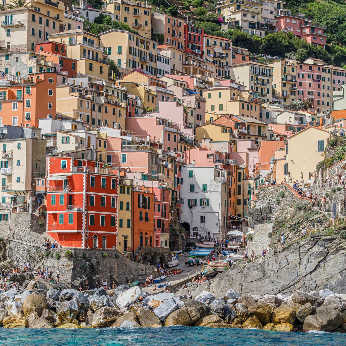 Colourful houses rise steeply above the rocky harbour and turquoise water of Riomaggiore on Italy’s Ligurian coast.