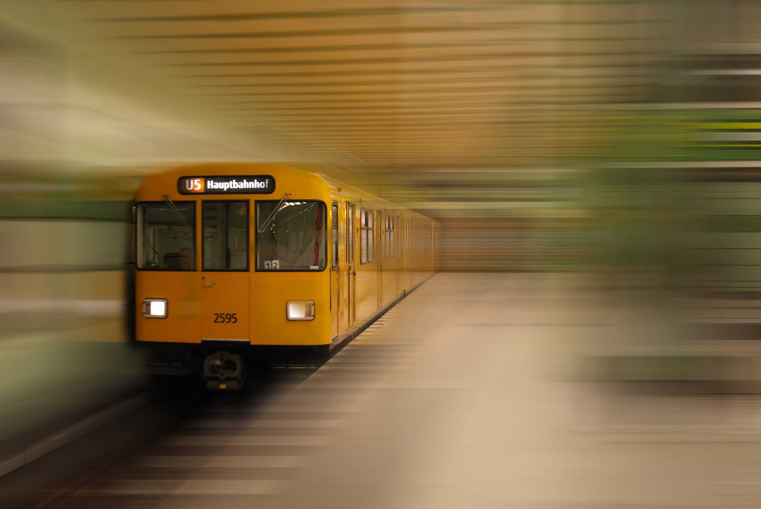 Yellow U5 underground train marked “Hauptbahnhof” approaches through a station, with the platform and background streaked by motion blur.