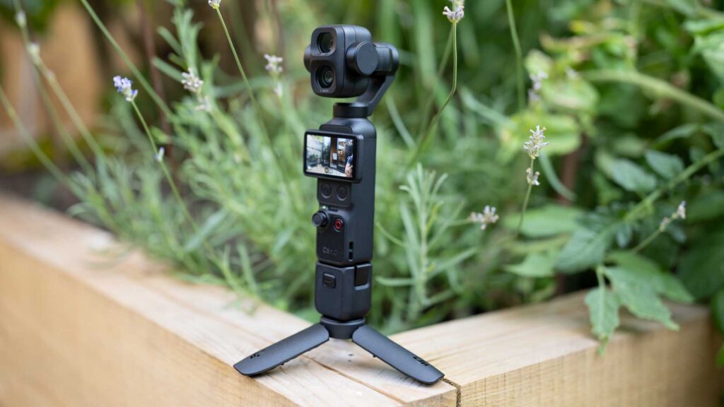 Front view of the DJI Osmo Pocket 4P on a small tripod, showing its two camera lenses against a leafy garden background.