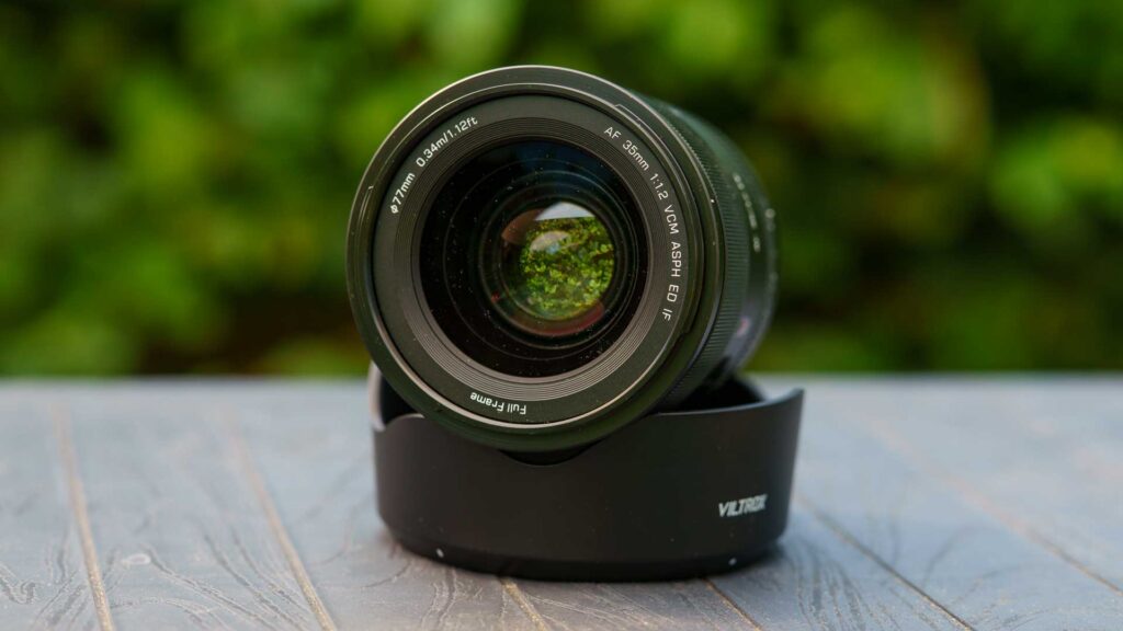 Front element of the Viltrox AF 35mm F1.2 LAB FE lens resting in its hood, with green foliage reflected in the glass.