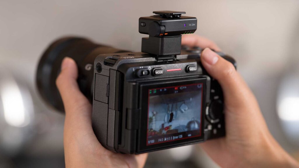 DJI Mic Mini 2S receiver mounted on a mirrorless camera’s hot shoe, with illuminated status lights and the rear screen displaying a recording.