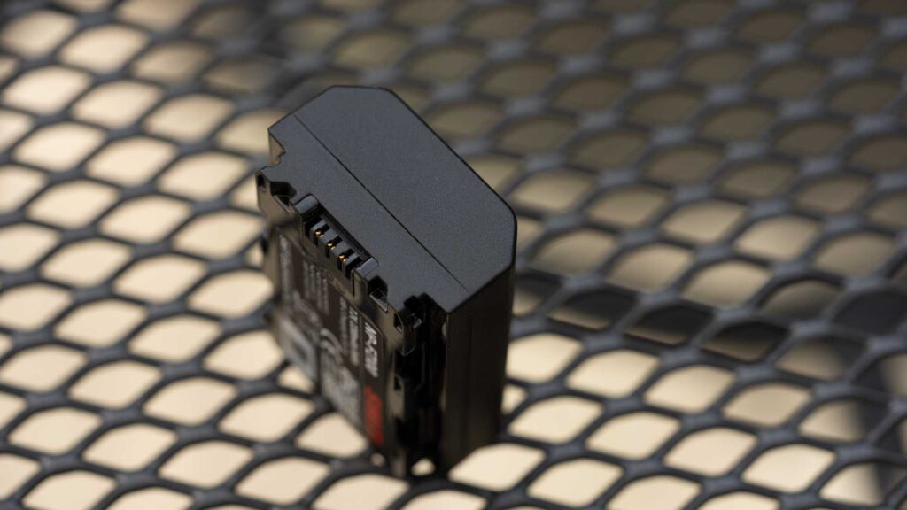 Swit PowerCell camera battery standing upright on a black metal mesh surface, showing its contact terminals and contoured casing.