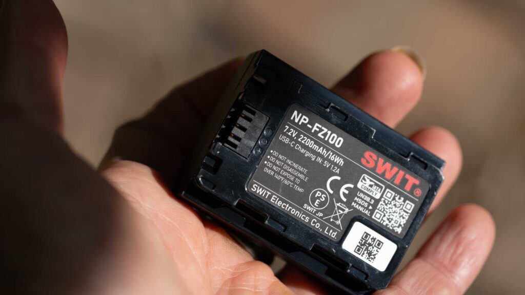 Swit NP-FZ100 PowerCell battery held in a hand, showing its 7.2V, 2200mAh/16Wh specification and USB-C charging information.