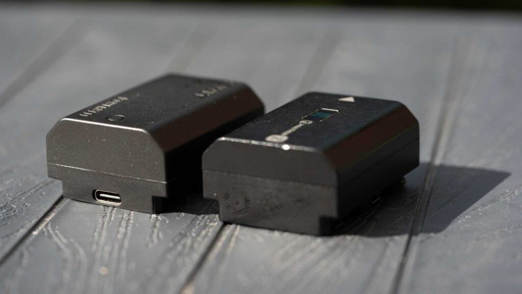 Swit PowerCell and Sony NP-FZ100 camera batteries side by side on a grey surface, with the Swit battery’s USB-C charging port visible.
