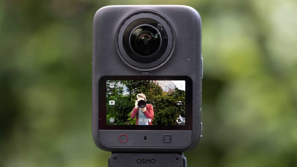 Front view of the DJI Osmo 360 II with its touchscreen showing a live view of a photographer and an 8K30 video setting.