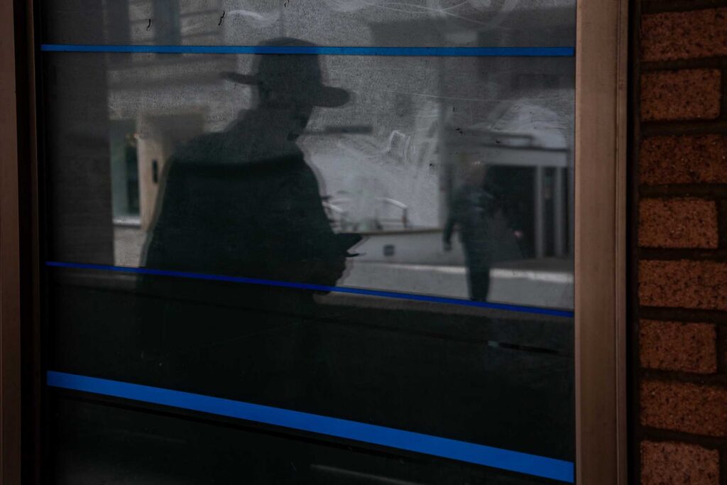 Reflection of a person in a wide-brom hat looking at a phone in dark glass crossed by bright blue horizontal lines.