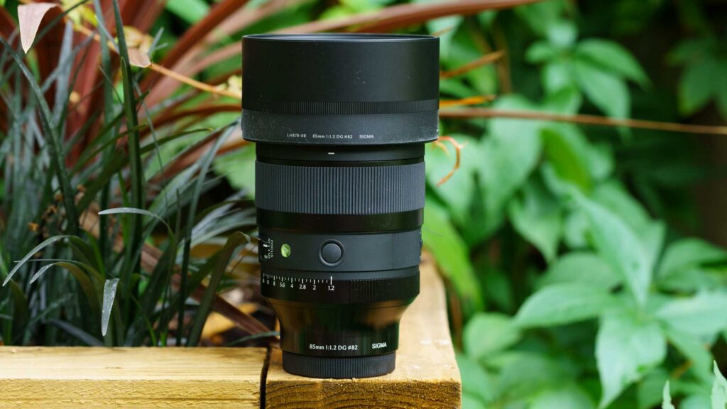 Side and top view of the Sigma 85mm f/1.2 DG Art on a Sony Alpha 7R V, showing the large hood and prominent barrel controls.