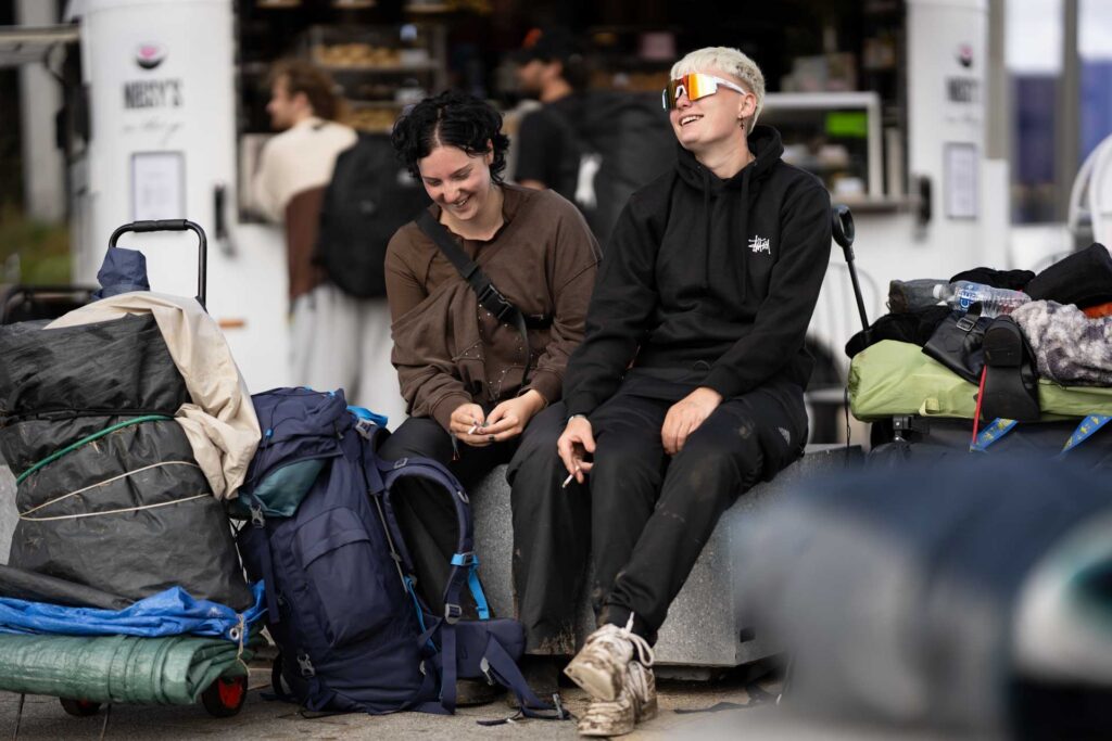 Two people sitting together and laughing beside bags and luggage, with a food kiosk softly blurred in the background.