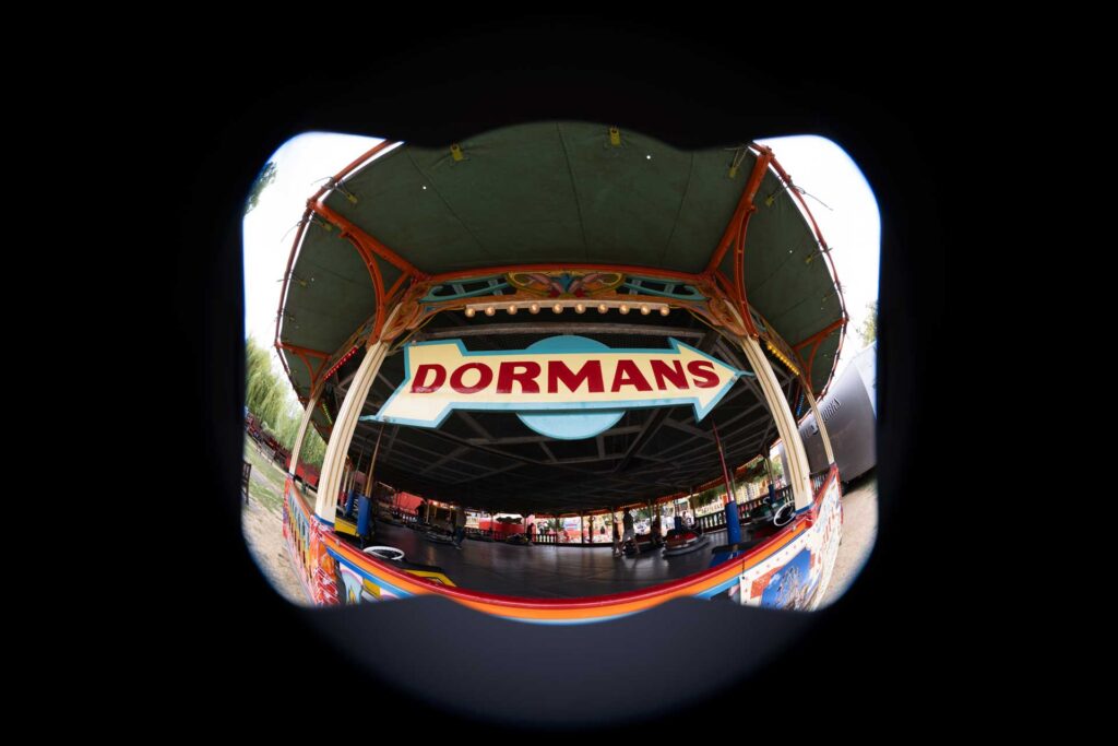 Circular fisheye view of the DORMANS dodgems pavilion surrounded by a large black border, with bumper cars visible inside.