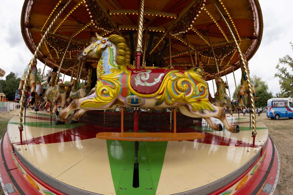 Colourful carousel horse photographed close-up, with ornate painted decoration and rows of illuminated bulbs curving overhead.