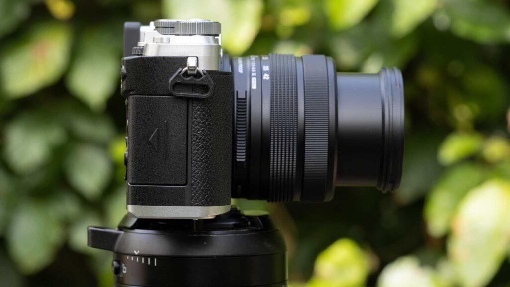 Side view of the OM System PEN on a tripod with its 14–42mm lens extended, showing the opposite side of the camera body.