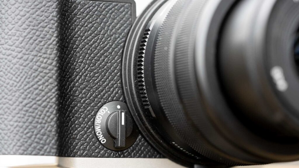 Close-up of the front of the OM System PEN showing the textured grip, lens mount area and Color/Mono selector switch.