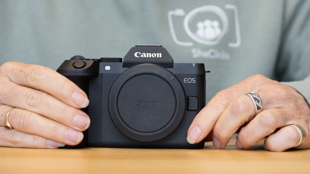 Front view of the Canon EOS R8 Mark II camera body with its body cap fitted, held between a reviewer’s hands on a table.