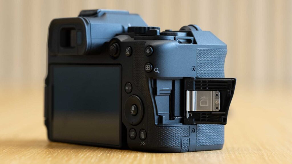 Rear three-quarter view of the Canon EOS R8 Mark II with its memory card compartment door open, revealing the card slot.
