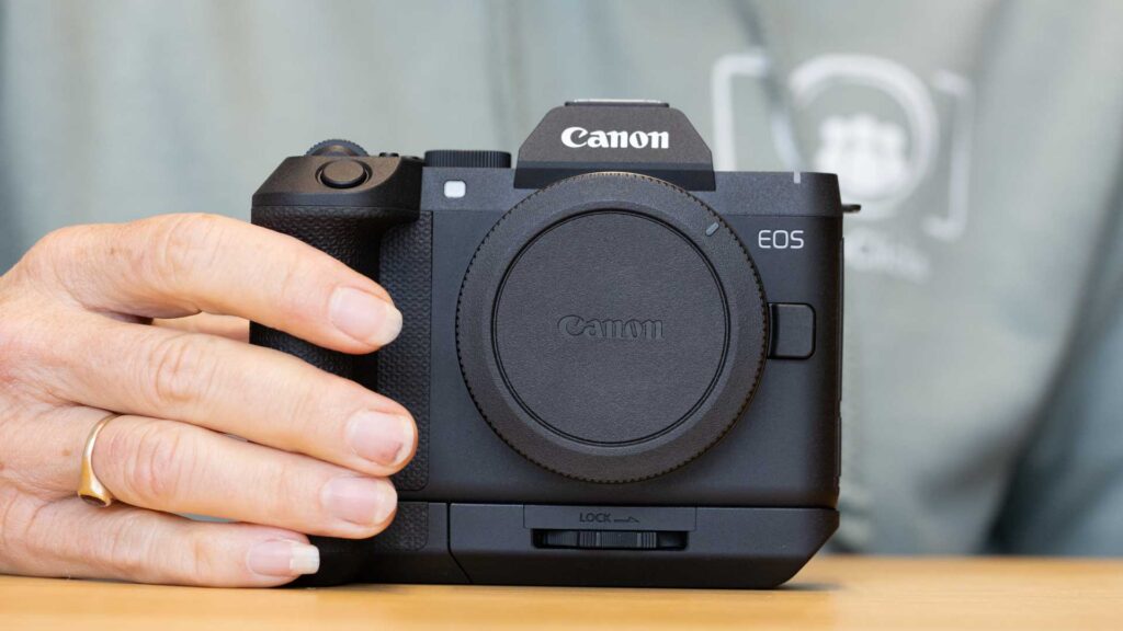 Front view of the Canon EOS R8 II with the extension grip fitted, held in one hand with a body cap covering the lens mount.