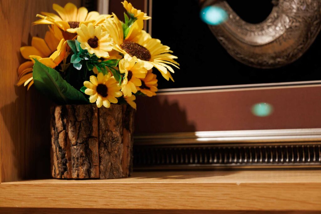 Yellow flowers in a rustic pot photographed in dim indoor light, with visible grain across the darker background.
