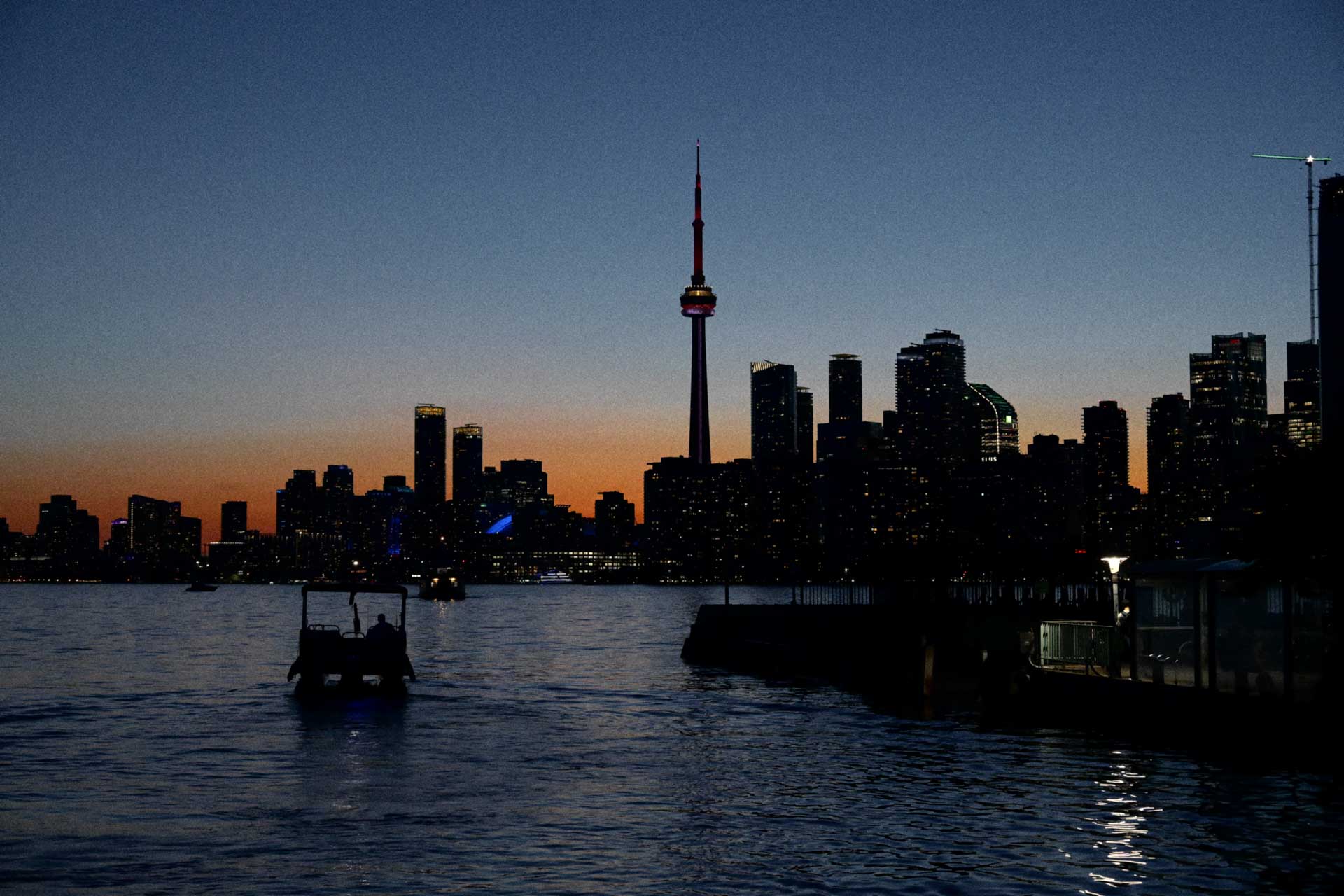Toronto’s skyline and CN Tower appear in silhouette across the water beneath an orange and blue dusk sk
