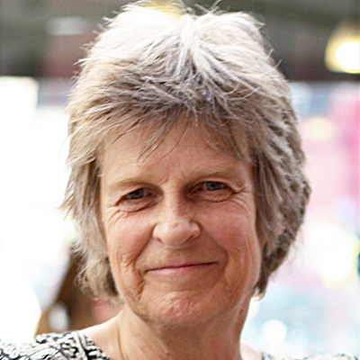 Close-up portrait of Sarah Wyld with short grey hair and a slight smile, against a softly blurred background.